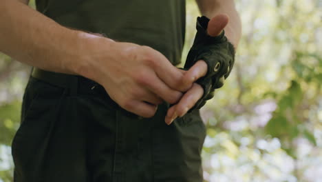 close up view of tourist removing fingerless glove, veins visible on hand and forearm, belt and cargo pants visible, dappled sunlight filtering through forest canopy casting highlights on skin