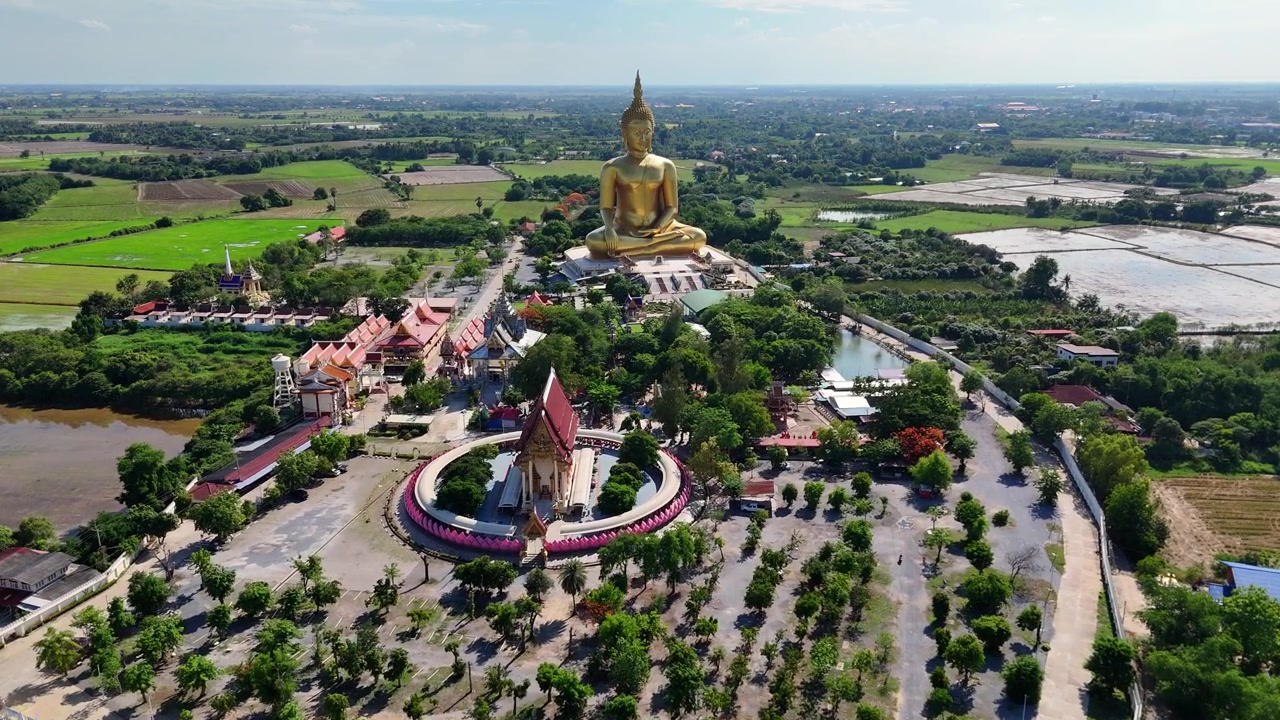 Góc nhìn từ trên cao, máy quay di chuyển vào để giới thiệu tượng Phật Vàng khổng lồ và ngôi đền Wat Muang tráng lệ ở Ang Thong, Thái Lan. Một khu du lịch được bao quanh bởi những cánh đồng lúa vào một ngày nắng đẹp.