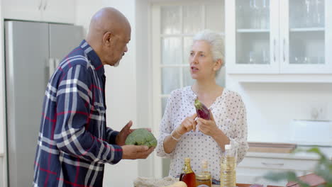 una pareja biracial feliz desempaquetando bolsas de compras en la cocina, en cámara lenta.