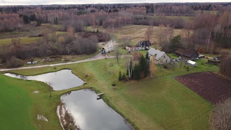 cierre lento y constante en una toma de drones de una antigua casa familiar en el campo rural junto a dos estanques y rodeada de bosques - día gris de otoño