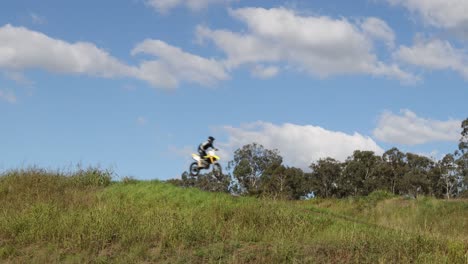 motorcyclist jumps over grassy hill under blue sky