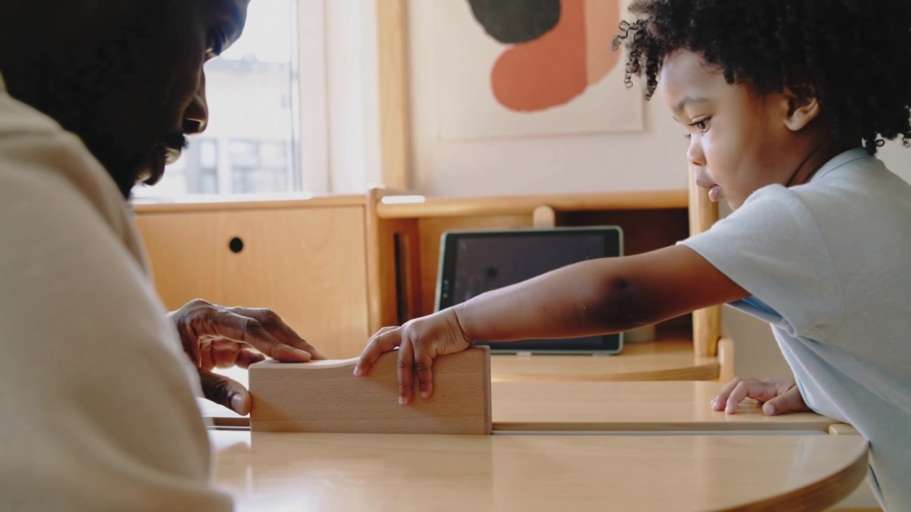 Placing dad wooden block at home table, toddler in short-sleeve top pushing for skills, copy space