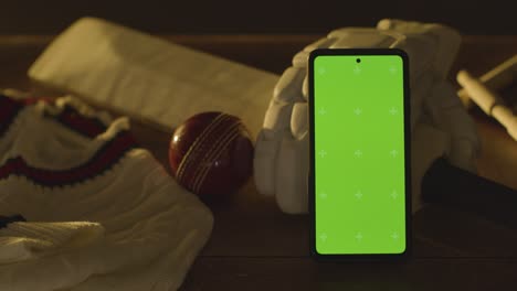 green screen mobile phone surrounded by cricket bat ball and clothing on wooden surface 1