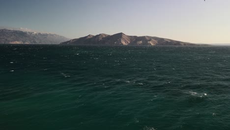 Toma-Aérea-Con-Un-Dron-Sobrevolando-El-Mar-Adriático-En-Croacia-Cerca-De-La-Playa-De-Baska-En-Un-Día-Soleado-Viendo-Una-Montaña-Imponente-En-El-Horizonte-4k-60fps