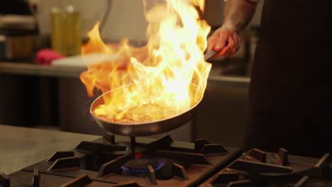 el chef trabaja hábilmente con sus manos, creando una llama controlada en una sartén caliente con aceite