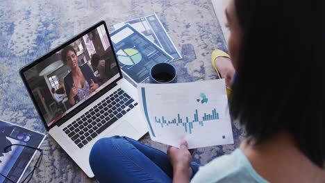 African-american-woman-holding-a-document-having-a-video-call-on-laptop-at-home