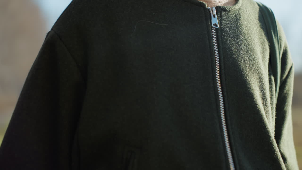 Close up of female hands with red nail polish near pocket of green jacket over beige sweater outdoors in natural daylight showing detail of casual clothing seasonal wear elements