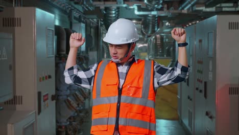Asian Male Engineer With Safety Helmet Screaming Goal And Dancing Celebrating In Engine Control Room, Work Of Electrical Generators