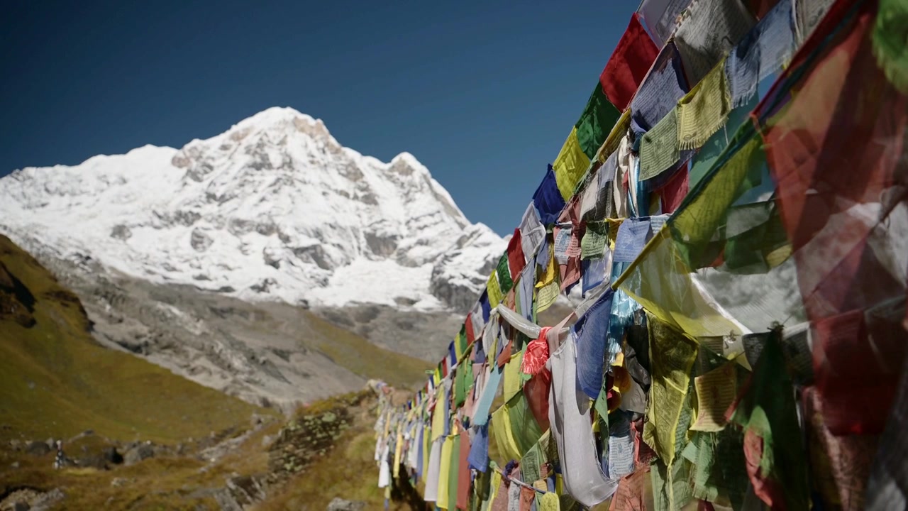 Himalajan vuoret ja rukousliput Nepalissa. Värikkäitä tiibetiläisiä rukouslippuja sinisellä, aurinkoisella taivaalla lumihuippuisilla Himalajan vuorilla Annapurnassa. Värikkäitä buddhalaisia lippuja lumisessa vuoristomaisemassa.