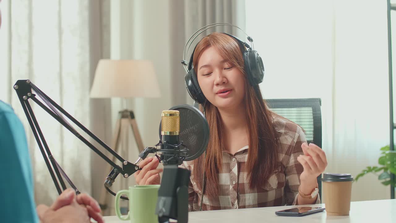 Over Shoulder View, Young Asian Woman In Headphones Singing Into Microphone While Recording Podcast With Male Host In Studio