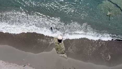 aerial shot of the shore of the beach in ocoa, young boy with big hat sitting enjoying the gentle waves of the sea