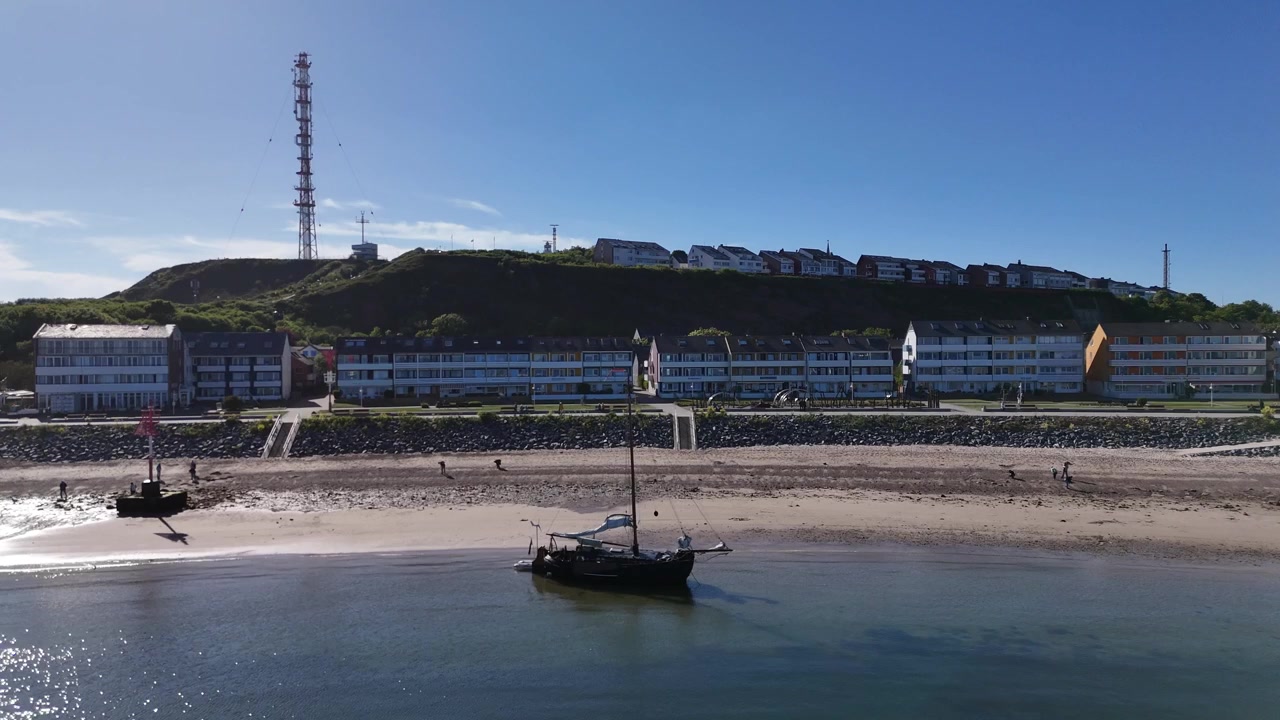 Veduta aerea della baia con una barca a vela a fondo piatto, case sulla spiaggia di Oberland e torri sullo sfondo.