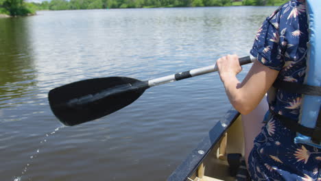 Young-woman-rowing-a-canoe-down-a-river-on-a-sunny-summer-day,-high-angle-shot,-slow-motion