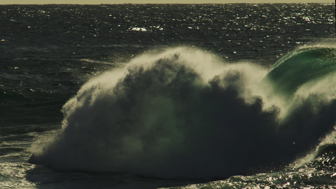 Clean wave peels forward in golden hour ocean glow with soft rolling spray and textured water