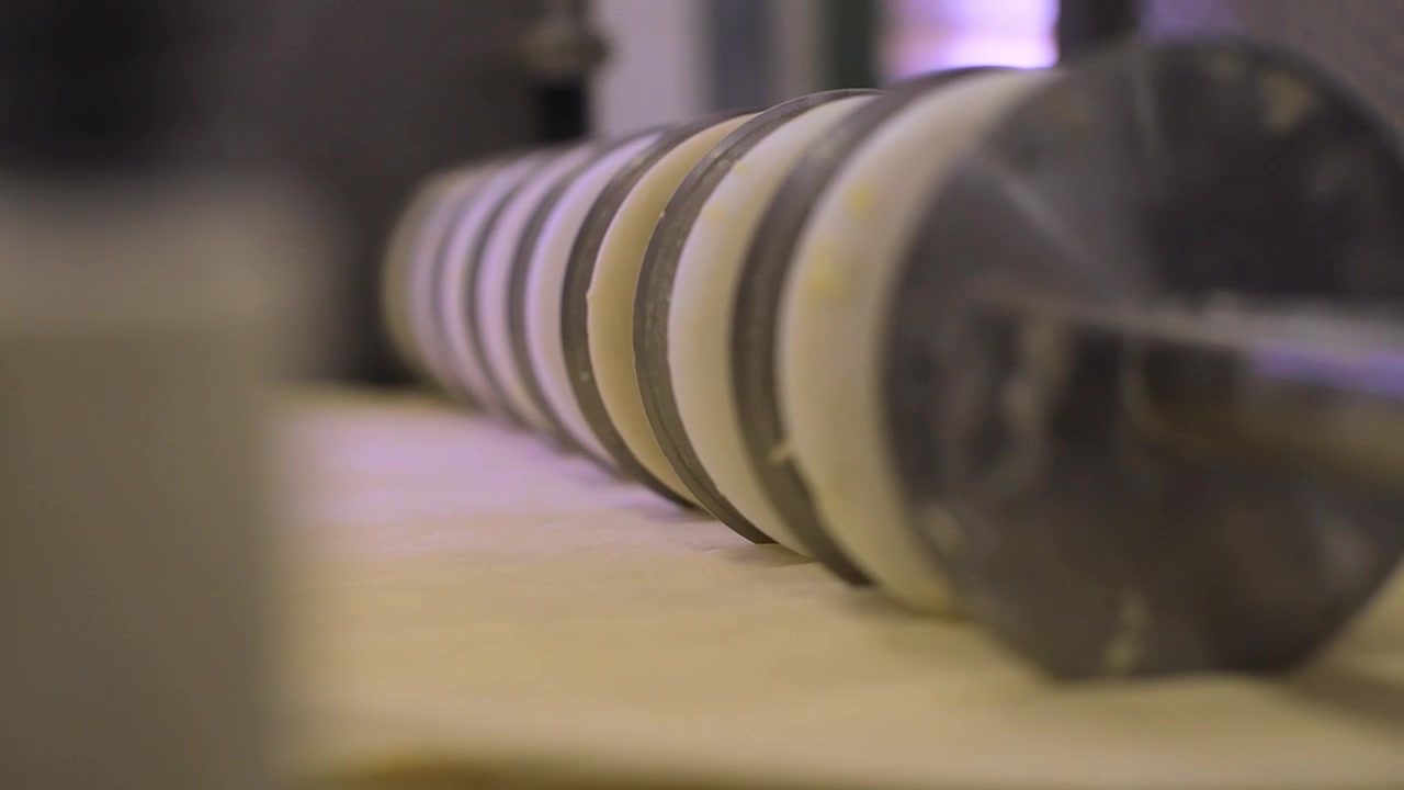 Runde industrielle Schneidemaschine schneidet große Mengen Rohrteig in einer Brotfabrik.