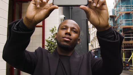 Male-taking-a-photo-on-his-smart-phone-on-a-street-in-London-City