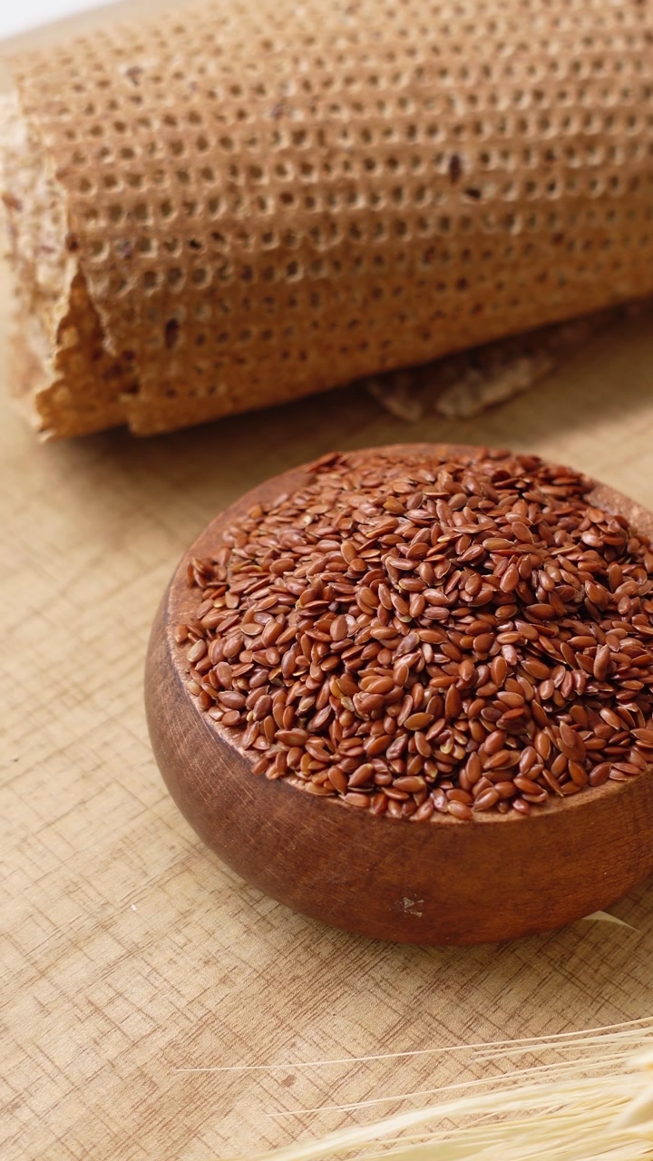 A Bowl of Flax Seeds on a Wooden Surface with Crispbread