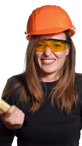 a beautiful woman in orange eyeglasses and helmet is holding a hammer in her hands and hitting herself by it in her hand on a white background in the studio. engineer vertical video