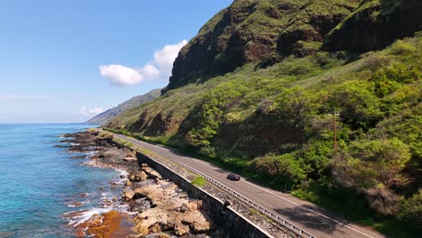 steep mountains and rocky coastline with a car on a highway in oahu, hawaii
