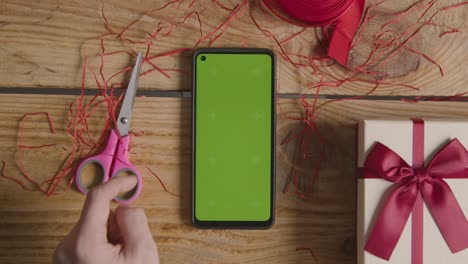 Fotografía-Cenital-De-Un-Hombre-Que-Envuelve-Un-Regalo-De-San-Valentín-Romántico-Presente-En-Una-Caja-Con-Un-Teléfono-Móvil-De-Pantalla-Verde