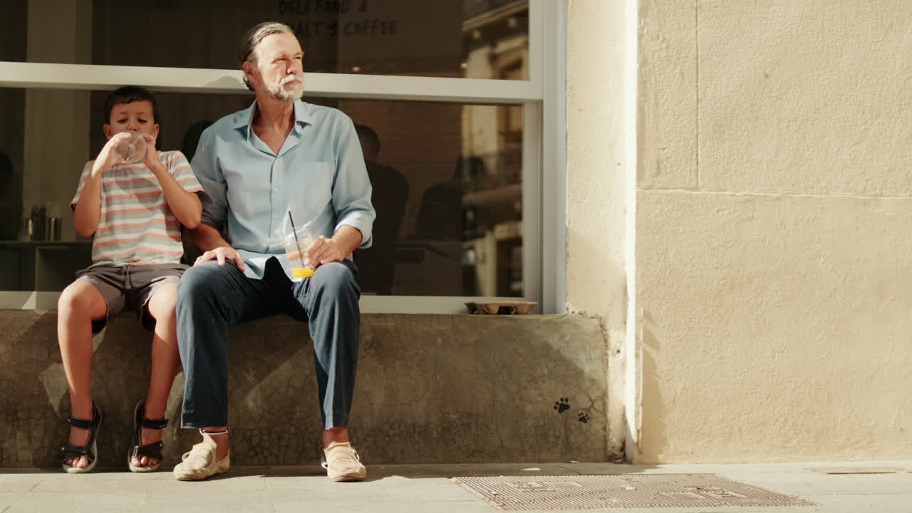 Grandfather and Grandson Sitting Outdoors and Drinking Beverages