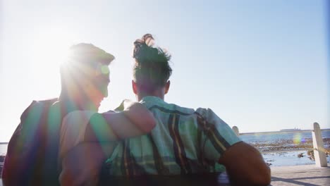 happy diverse gay male couple sitting on bench and embracing at promenade by the sea, slow motion