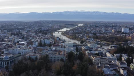 aerial flying over kutaisi city with snowy mountains and river