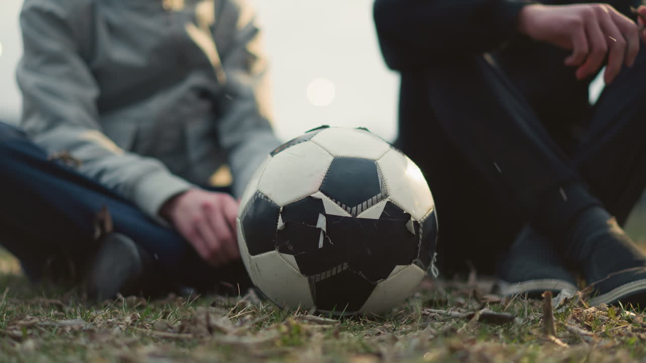Close-up of a soccer ball on a grassy field with a blurred view of two people seated behind