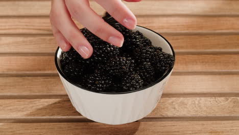 woman's hand picking blackberries from a bowl