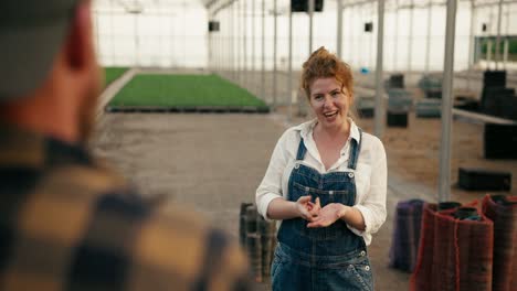 Over-the-shoulder-a-confident-girl.-A-farmer-with-red-hair-talks-with-a-guy-in-a-checkered-shirt-about-working-in-a-greenhouse-on-a-farm