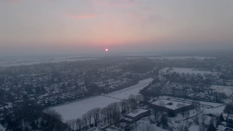 Aerial-overview-of-beautiful-small-town-covered-in-snow-at-dawn---drone-flying-backwards