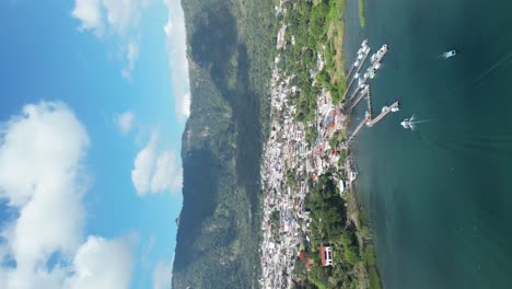 vista de retrato de avión no tripulado en guatemala volando sobre un lago azul rodeado de montañas verdes y volcanes en un día soleado en aitlan