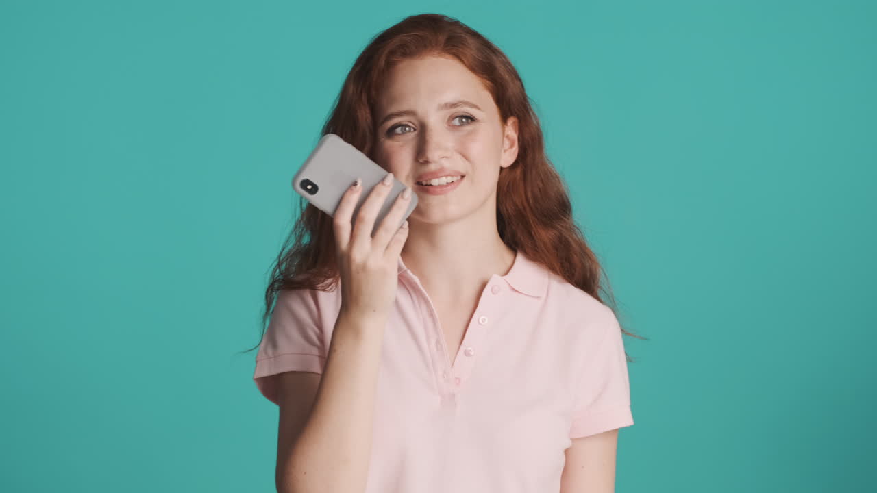 Redheaded girl in front of camera on turquoise background.