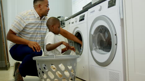 side view of mid adult black father and son washing clothes in washing machine at comfortable home 4