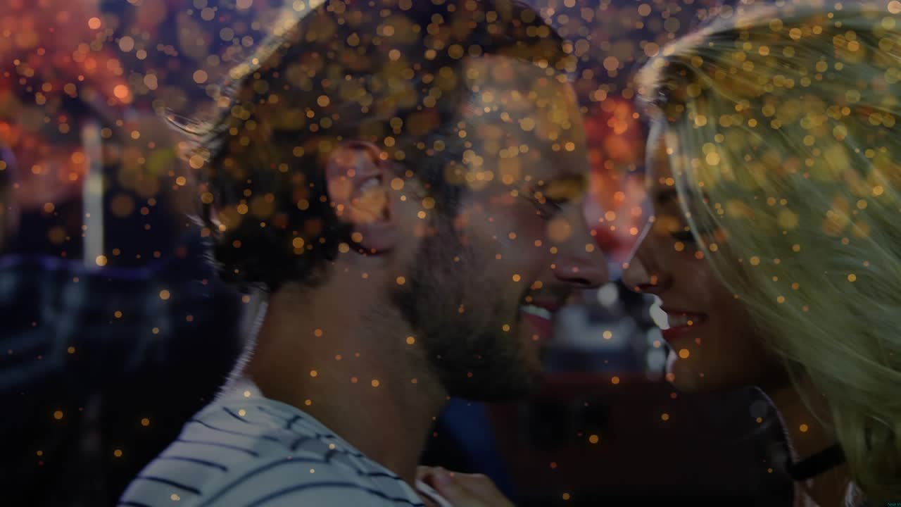 Mand og kvinde smiler og læner sig ind i klubben, kvinden rører brystet, gylden bokeh fremhæver intimiteten