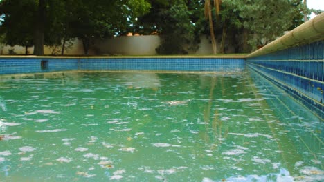 una piscina sucia con azulejos azules brillantes llenos de polvo de choque blanco flotando en la superficie - toma amplia