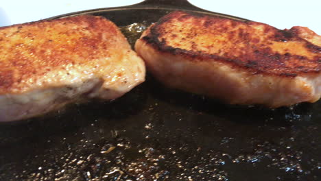 closeup of delicious looking pork chops frying in a cast iron pan at high heat