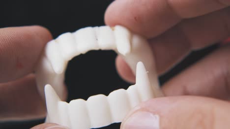 man holds toy vampire teeth on black background macro