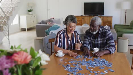 una pareja de ancianos afroamericanos sentados a la mesa haciendo rompecabezas bebiendo té