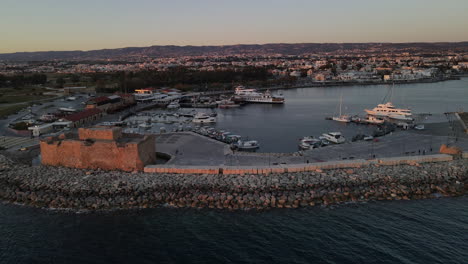 Drone-orbit-of-Pafos-Castle-bathed-in-warm-sunset-hues,-overlooking-the-harbor,-Cyprus