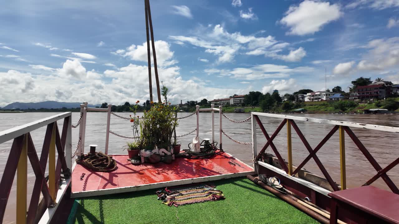 Slow boat traveling along the Mekong River, passing Houayxay town under a blue cloudy sky
