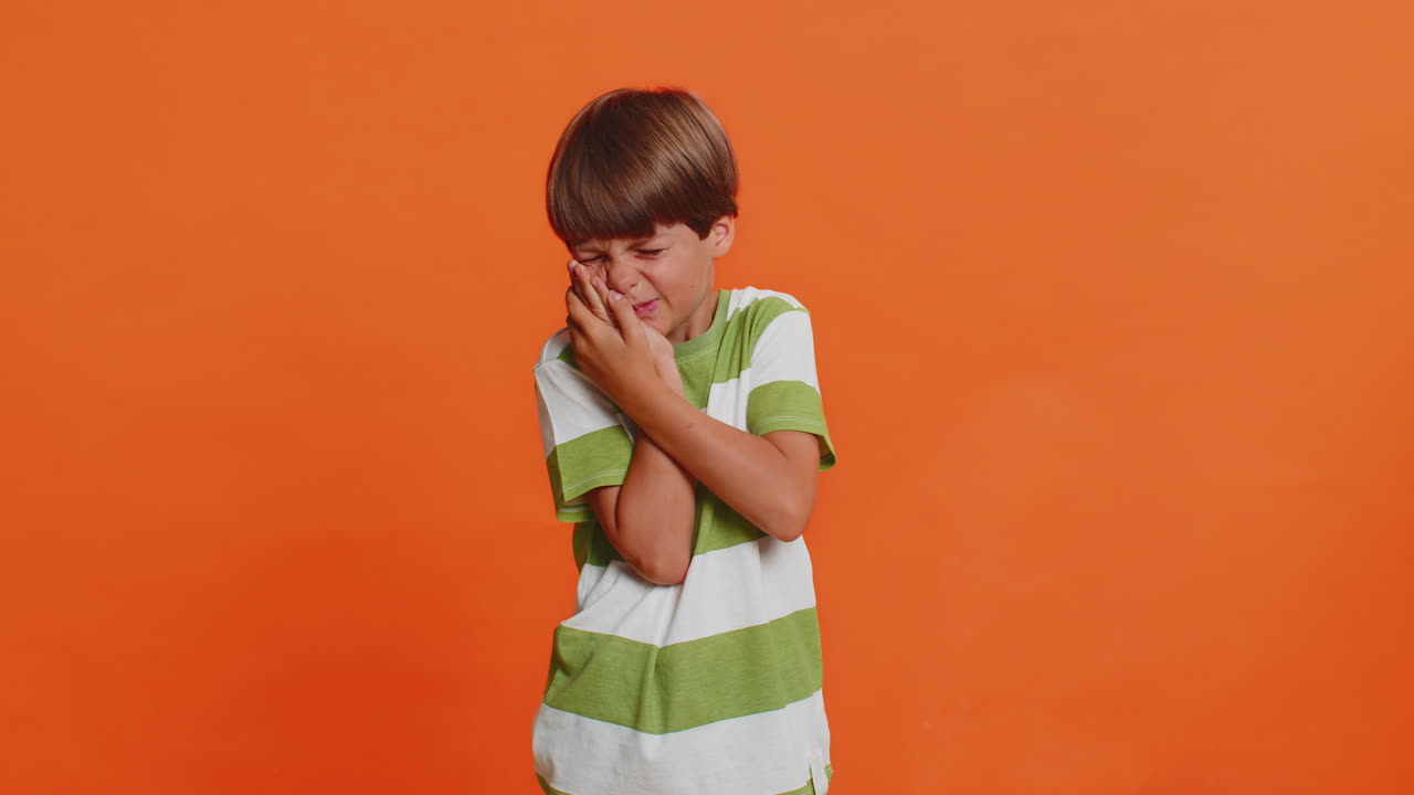 niño niño tocando la mejilla cerrando los ojos con expresión de terrible sufren de doloroso dolor de dientes