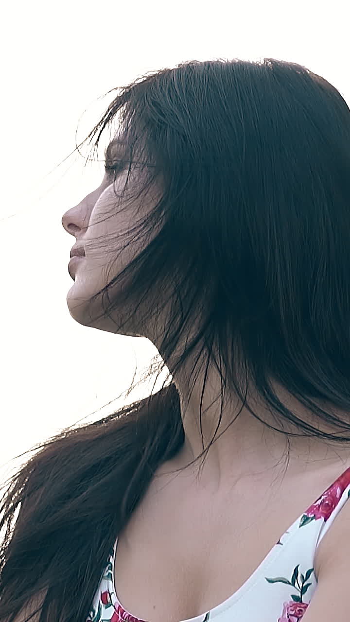closeup young brunette woman with loose flowing hair in summer dress shakes head and fixes hair slow motion