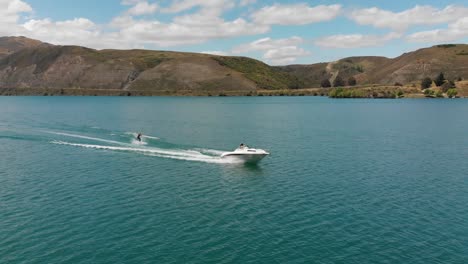 cámara lenta: esquí acuático detrás de un bote en el lago dunstan cerca de la represa clyde, otago central, nueva zelanda con montañas y nubes en el fondo