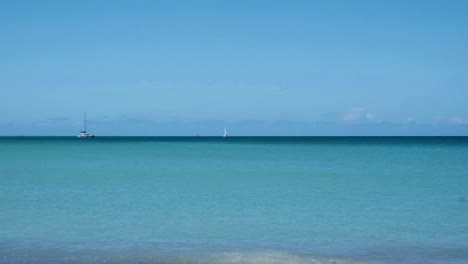 sailing catamaran crosses the horizon over tropical blue and turquoise waters in the caribbean