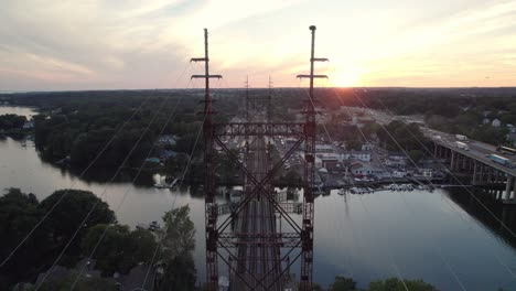 drone disparado moviéndose hacia adelante sobre las vías del tren con cables, puesta de sol y interestatal en el fondo