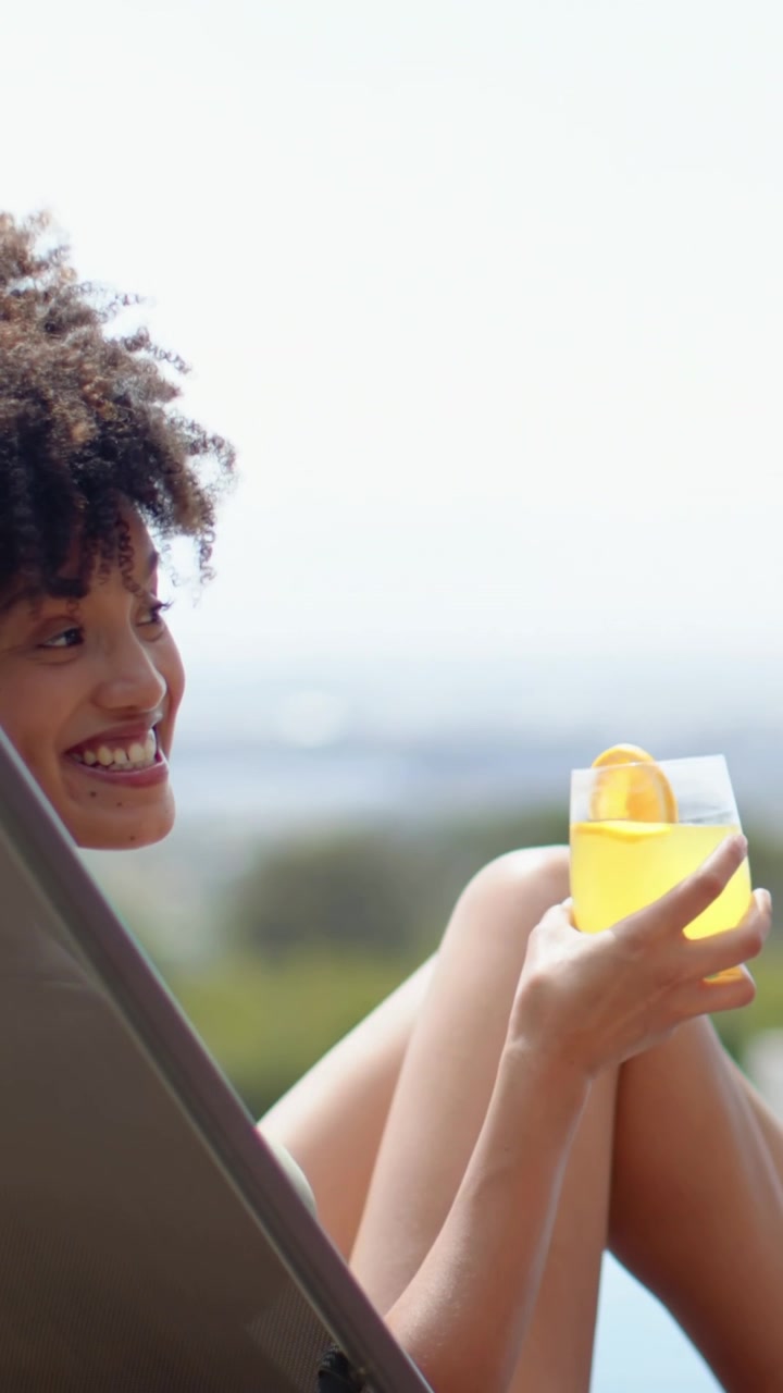 Vertical video: Camera zooming urging woman in green bikini rising on pool lounger holding lemonade