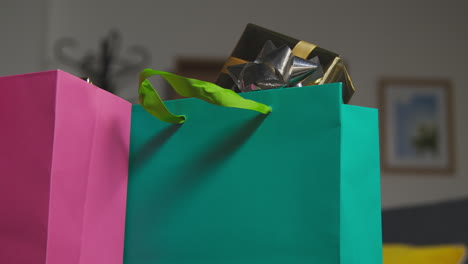 close up of man putting down gift wrapped presents in colourful bags with tag on table in lounge at home