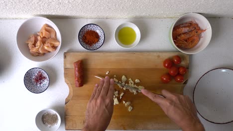 veiny male hands chopping garlic into pieces on wooden cutting board