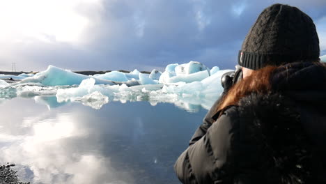 toma cinematográfica de una mujer tomando fotos del paisaje y los icebergs encontrados en el parque nacional jökulsárlón en islandia